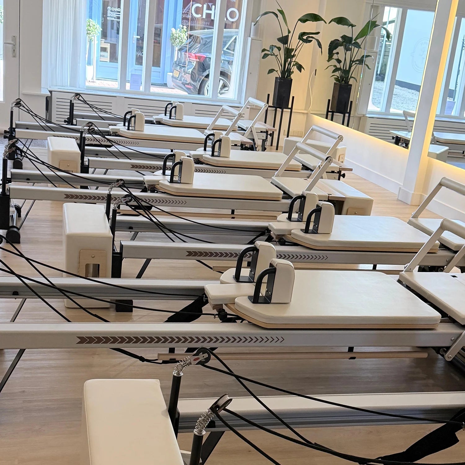 Pilates reformers lined up in a studio with large windows.